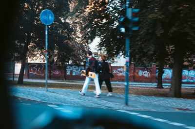 Man and woman walking on street by trees