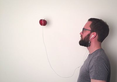 Side view of man with headphones attached to apple on white wall