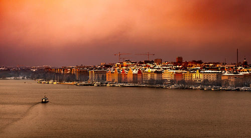 Sea by buildings against sky during sunset
