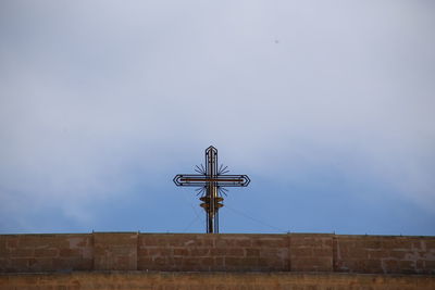 Low angle view of cross on wall against sky
