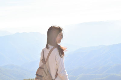Smiling woman looking away while standing against mountains and sky