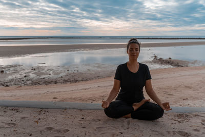 Portrait of young woman sitting at beach against sky