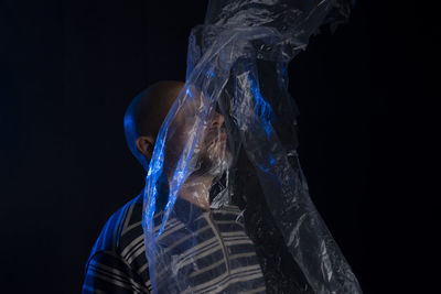 Mature man with a transparent plastic blue bag flying over his head and face. suffocate. 