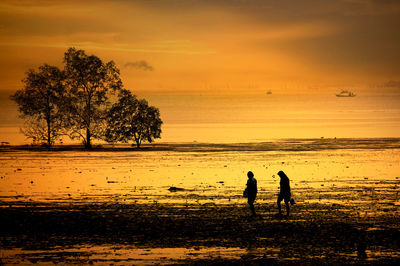 Silhouette people on sea against sky during sunset