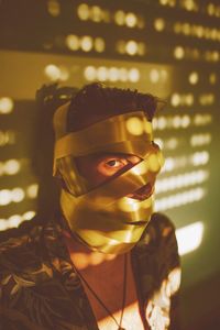 Close-up portrait of young woman wearing mask standing against wall at home