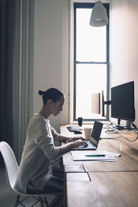 Side view of businesswoman using laptop computer while sitting at desk in office