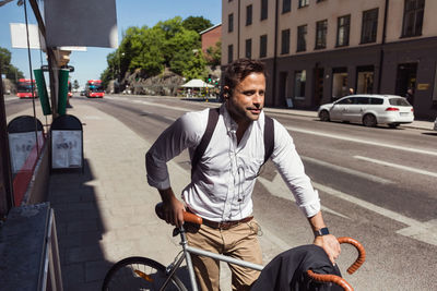 Thoughtful businessman standing with bicycle on sidewalk in city