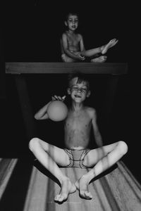 Shirtless boy looking at brother holding balloon in darkroom