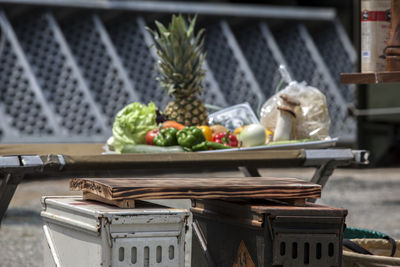 Cutting board on metal containers by fruits and vegetables on table during camping