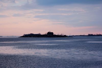 Hill in baltic sea against cloudy sky during sunset