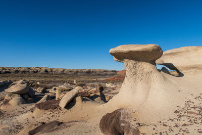 Rocks on sand against clear blue sky