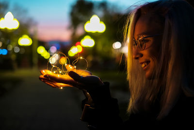 Portrait of smiling young woman holding illuminated outdoors