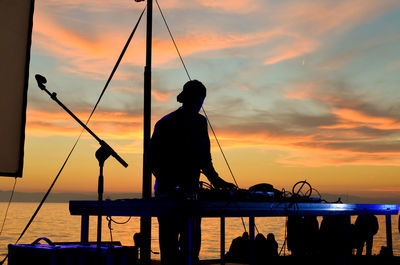 Silhouette man fishing in sea against orange sky