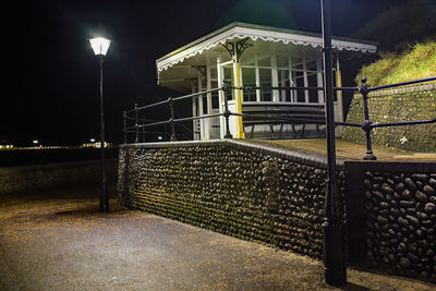 Illuminated street light by building against sky at night