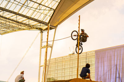 Low angle view of men on cable against sky