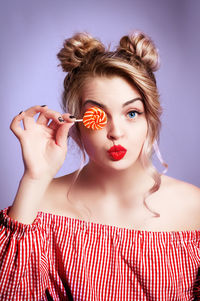 Portrait of beautiful young woman holding lollipop against purple background