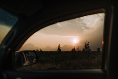 Scenic view of landscape against cloudy sky in grand teton national park during sunset seen through car window