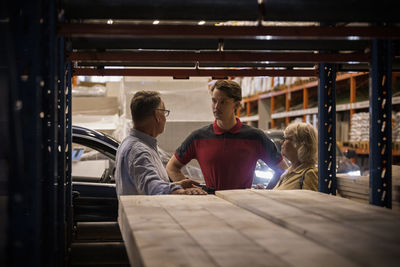 Senior male and female customer talking to salesman seen through rack at hardware store