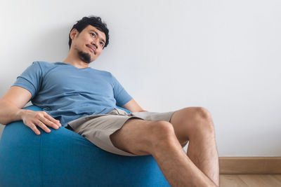 View of man's legs on white bed with tv and plant.