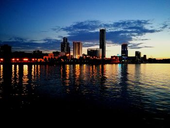 River by illuminated city buildings against sky