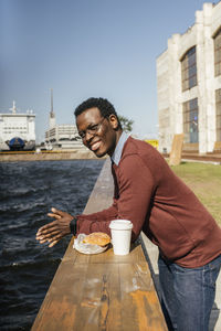 Young man looking at the sea, with eating hamburgerand coffee on railing