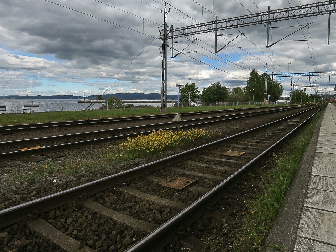 railroad track, rail transportation, public transportation, transportation, sky, railroad station, railroad station platform, cloud - sky, railway track, power line, train - vehicle, electricity pylon, cloudy, power supply, diminishing perspective, cloud, cable, vanishing point, day, travel