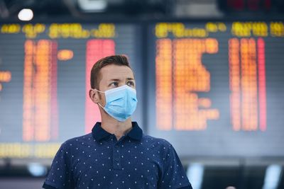 Man wearing face mask against airport departure board. 