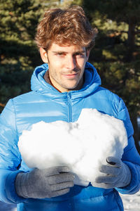 Young man holding heart shape snow during winter