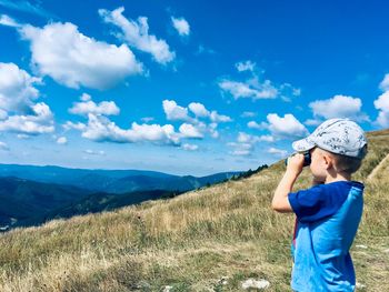 Boy looking though binoculars while standing on mountain