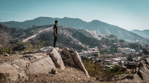 Young man standing on rock against sky