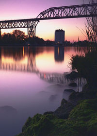 Silhouette bridge over river against sky during sunset