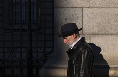 Side view of adult man in hat and leather jacket walking against wall on street. madrid, spain