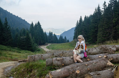 Woman sitting on street amidst trees against sky