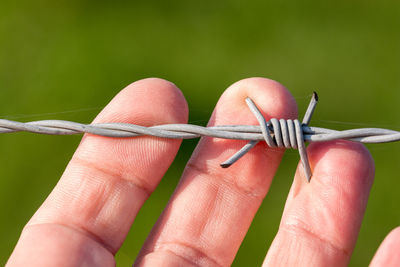 Close-up of hand holding barbed wire fence