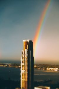 Rainbow over city buildings against sky during sunset