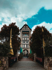 Footpath amidst trees and buildings against sky