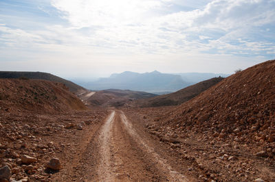 Dirt road amidst mountains against sky