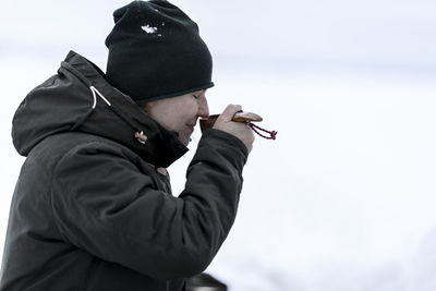 Side view of man holding cigarette against sky