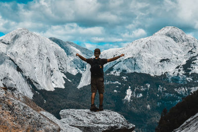 Rear view of man with arms outstretched standing on rock against mountains