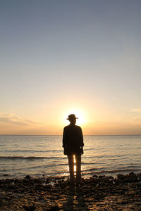 Rear view of silhouette man standing on beach during sunset