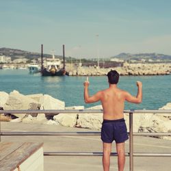 Rear view of shirtless man standing by railing 