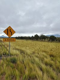 Road sign on field against sky