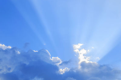 Low angle view of sunlight streaming through clouds