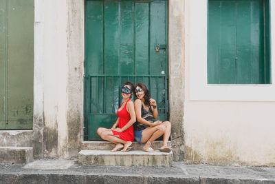 Portrait of two beautiful and happy girls sitting against a green colored door.