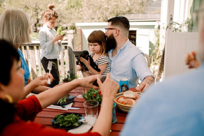 Multi-generational family having food while daughters using technology at patio