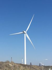 Low angle view of wind turbines on field against clear blue sky