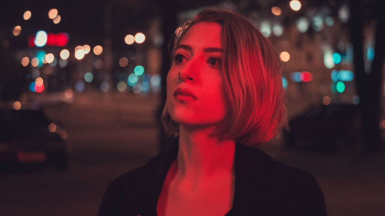 PORTRAIT OF WOMAN LOOKING AWAY AT ILLUMINATED CITY