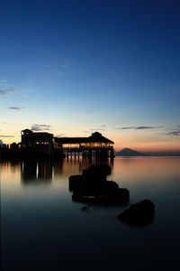 Silhouette built structure in sea against sky at sunset