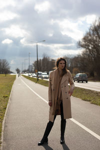 Portrait of young woman standing on road against sky