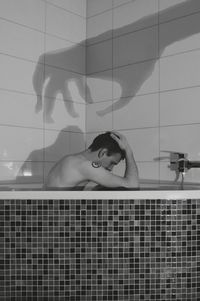 Shadow over shirtless man sitting in bathtub at home